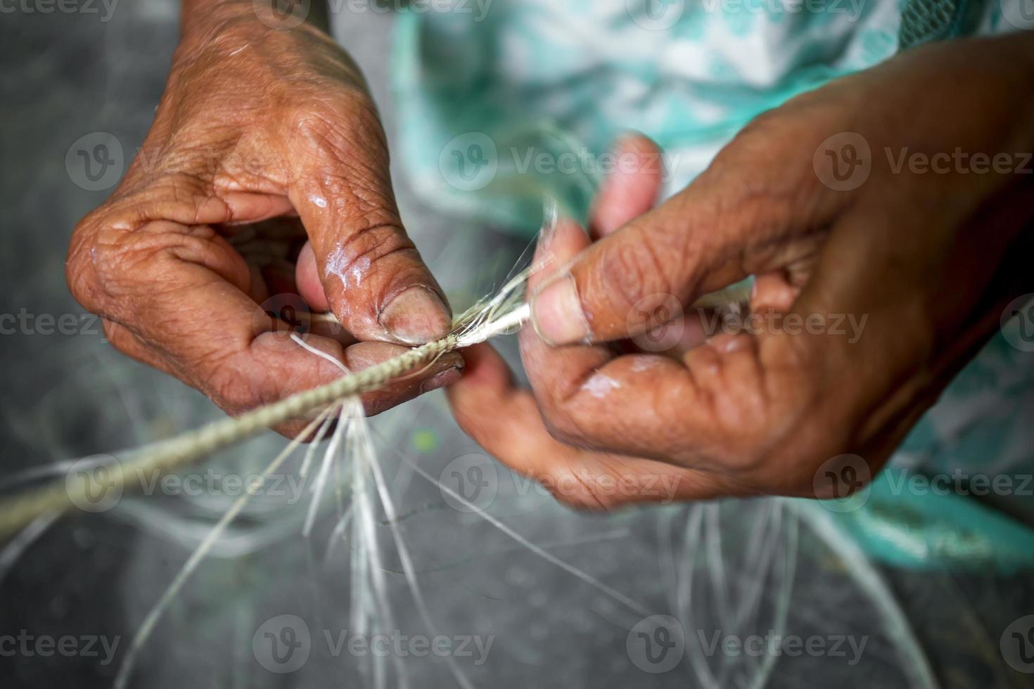 un antiguo años mujer es haciendo en su flaco manos un cuerda desde el plátano árbol fibra a madhupur, tangail, bangladesh foto