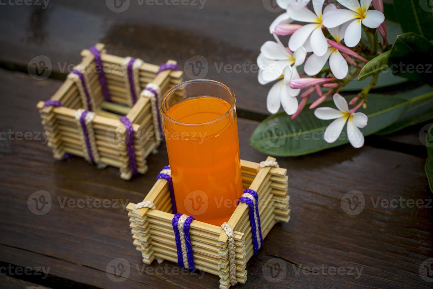 un vaso de naranja jugo con agua vaso poseedor hecho de bambú palos y fibra. decorativo de madera mesa con hermosa plumeria flores bambú vaso poseedor. foto