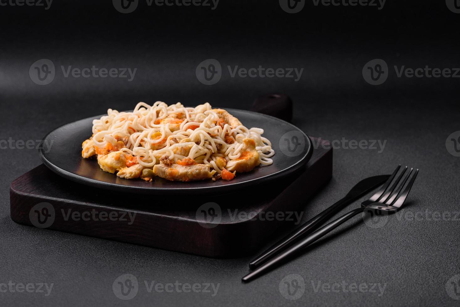Delicious noodles with chicken and vegetables or udon on a black ceramic plate photo