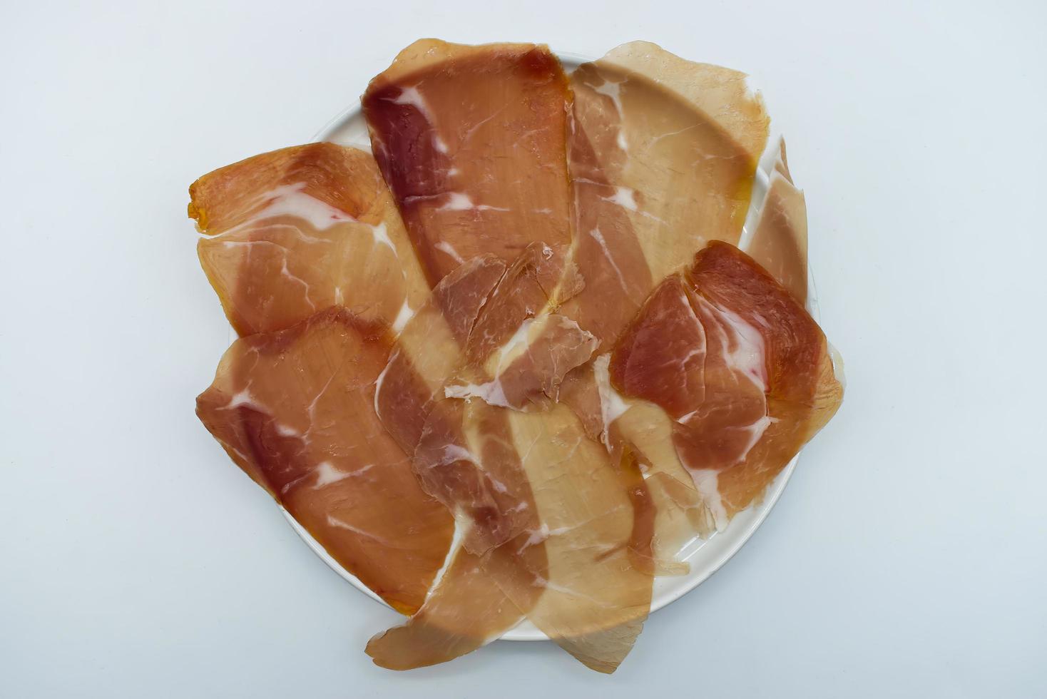 Slices of Italian prosciutto di parma, Italian ham, in a white dish isolated on white. Top view photo