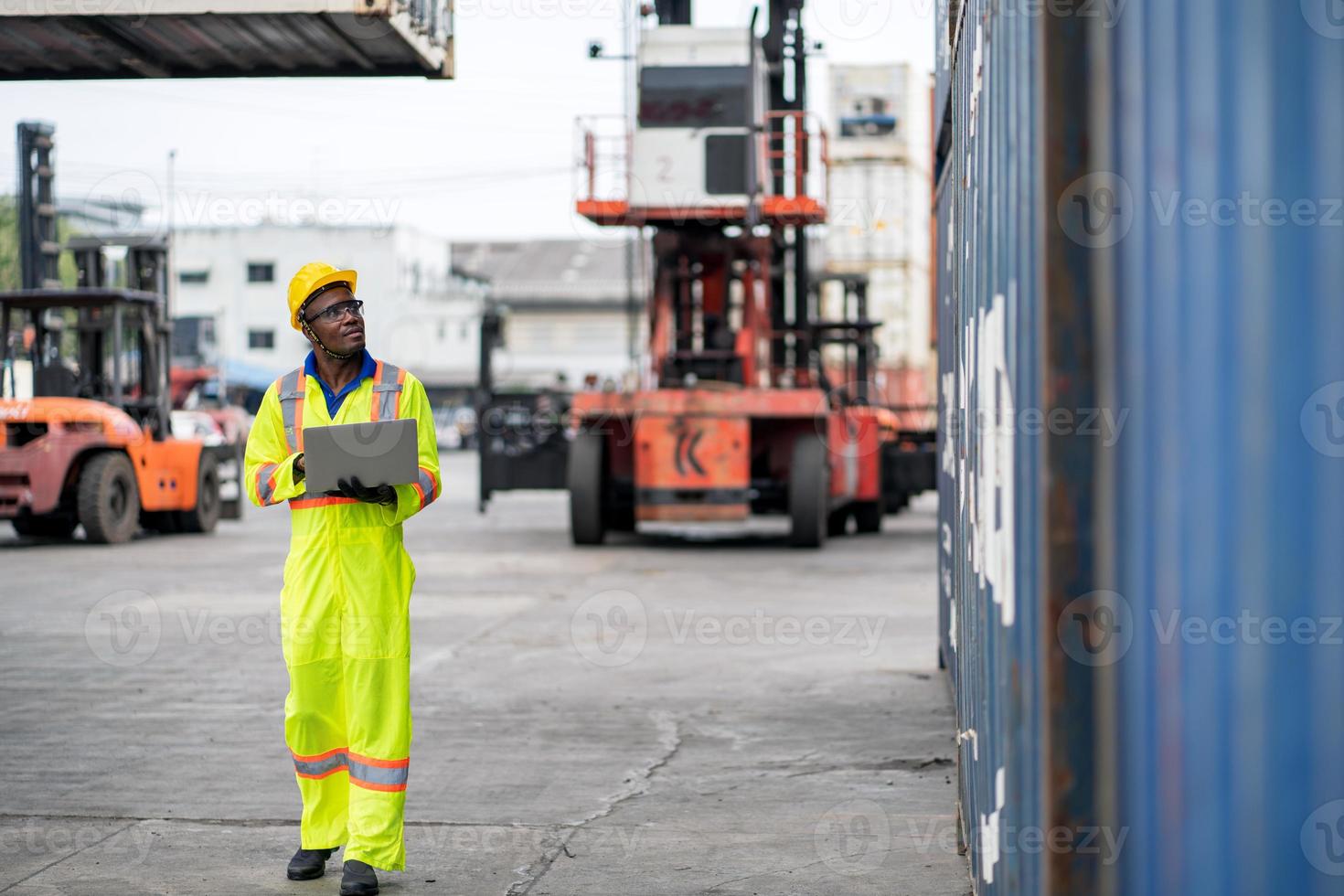 African technician dock worker in protective safety jumpsuit uniform and with hardhat and use digital tablet at cargo container shipping warehouse. transportation import,export logistic industrial photo