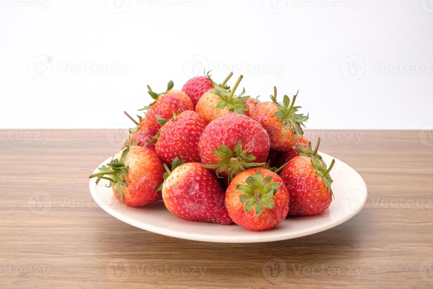 grupo de rojo fresas en blanco cuenco en de madera escritorio, sabroso postre, cerca arriba. foto