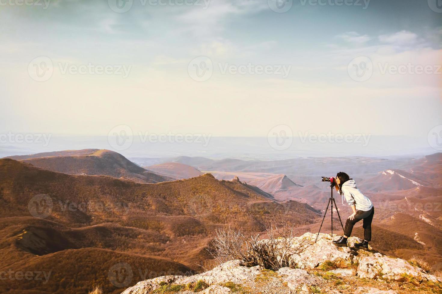 Young passionate attractive caucasian hipster woman content creator photographing mountains with red girly DSLR camera on tripod photo