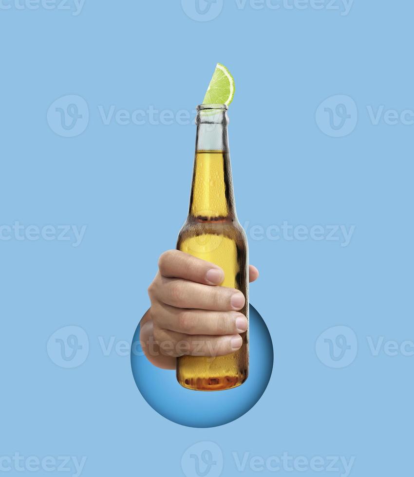 hand holding Mexican beer bottle with lime slice on light blue background photo