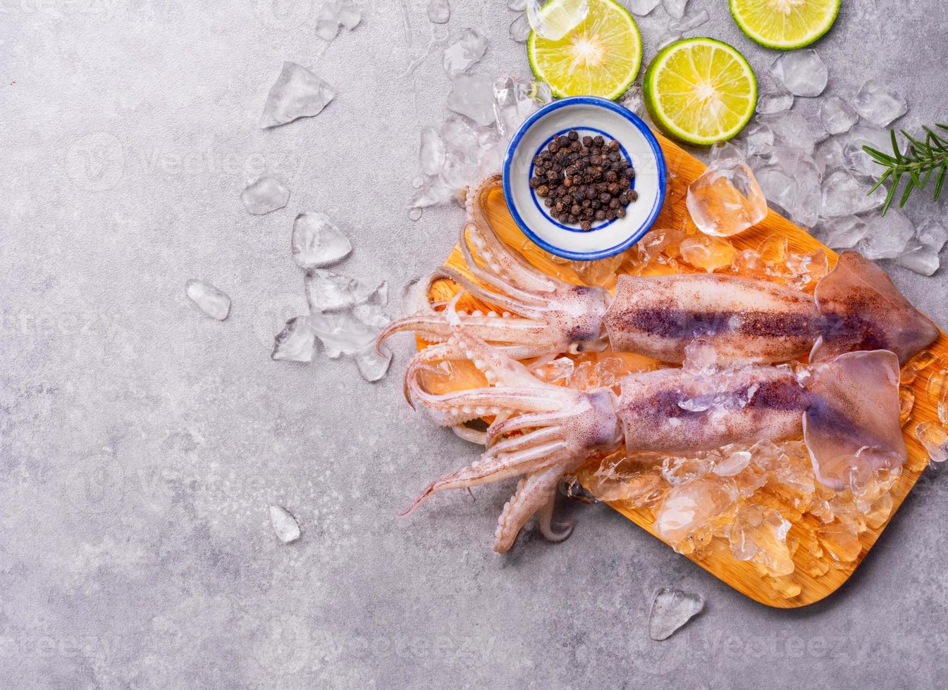 Raw squid on ice with lemon garlic spice salad on black wooden table background, fresh squid for cooked food at a kitchen restaurant or seafood market photo