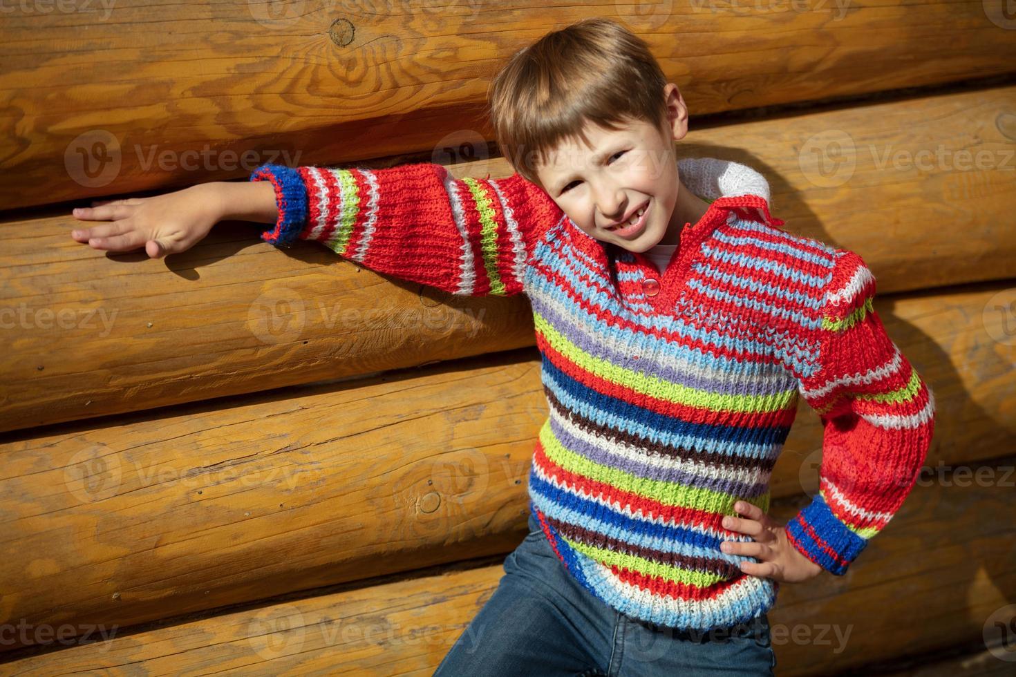 A boy of elementary age in a striped sweater on a background of a wooden fence. photo