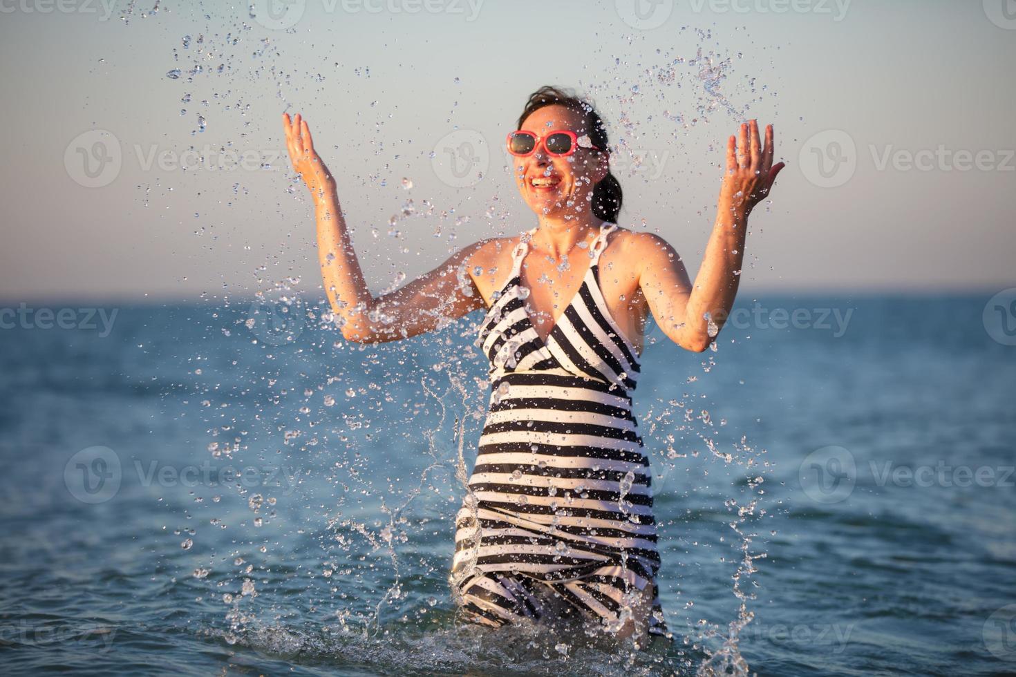 A happy elderly woman at sea. Splash sea water on vacation. photo