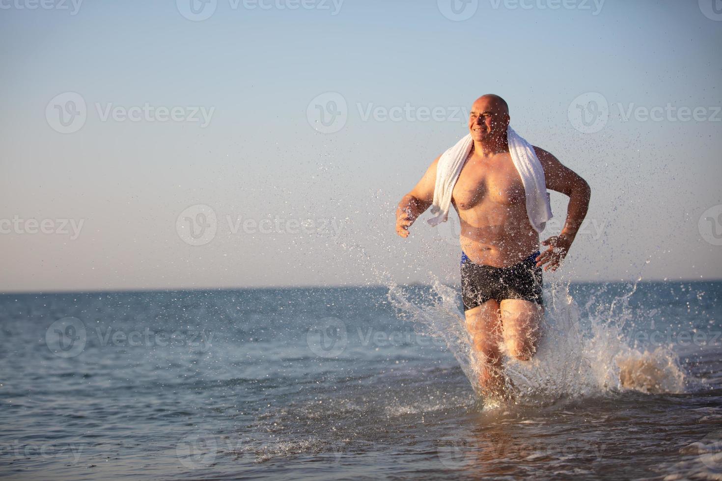 An elderly man runs along the beach. photo