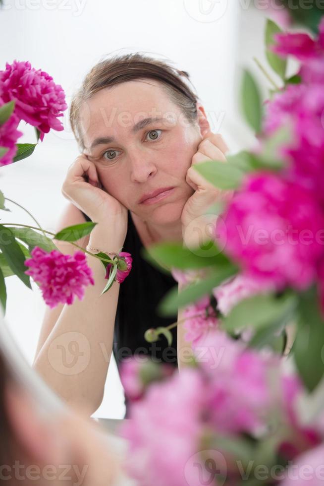 triste de edad mediana mujer mira en el espejo. foto