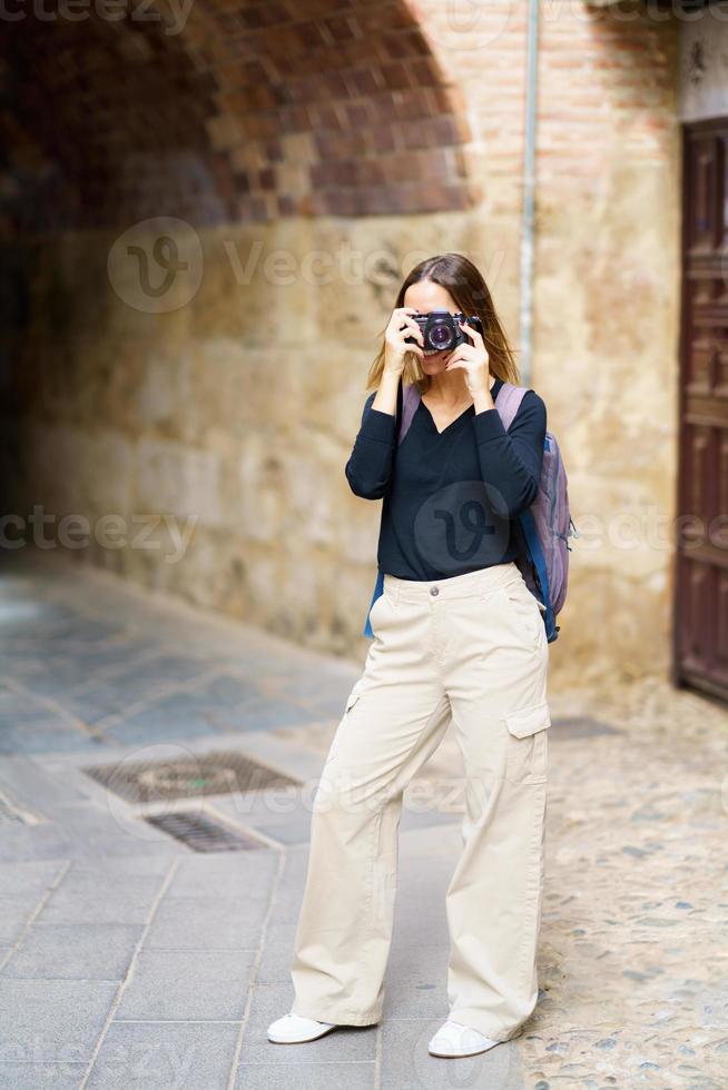 Content woman taking photos on camera near arched passage in old town