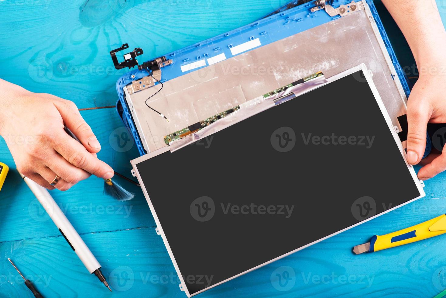 el asistente repara la computadora portátil con herramientas y manos en la mesa de madera azul. vista superior foto