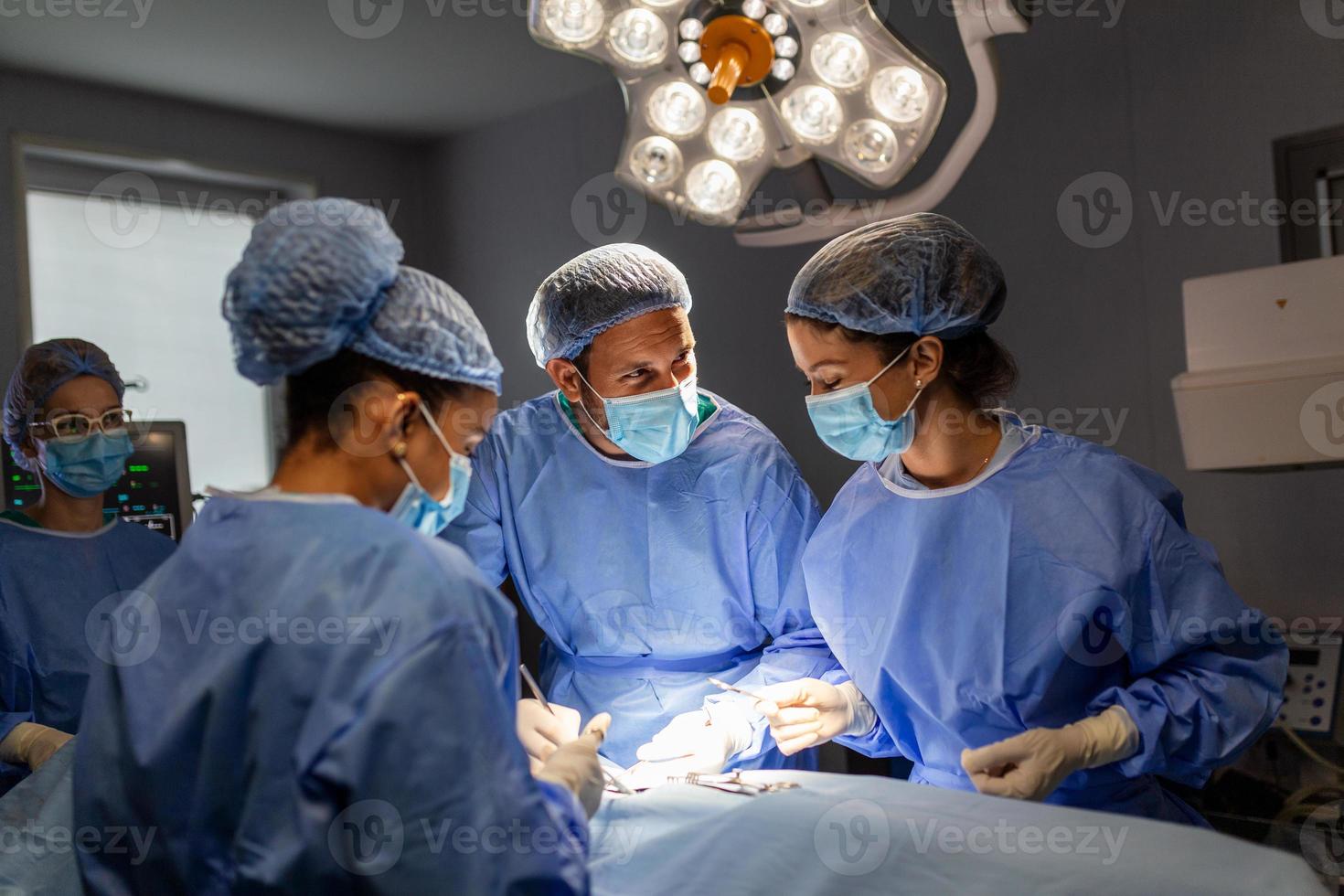 equipo diverso de cirujanos profesionales, asistentes y enfermeras que realizan cirugía invasiva en un paciente en el quirófano del hospital. los cirujanos hablan y usan instrumentos. verdadero hospital moderno. foto