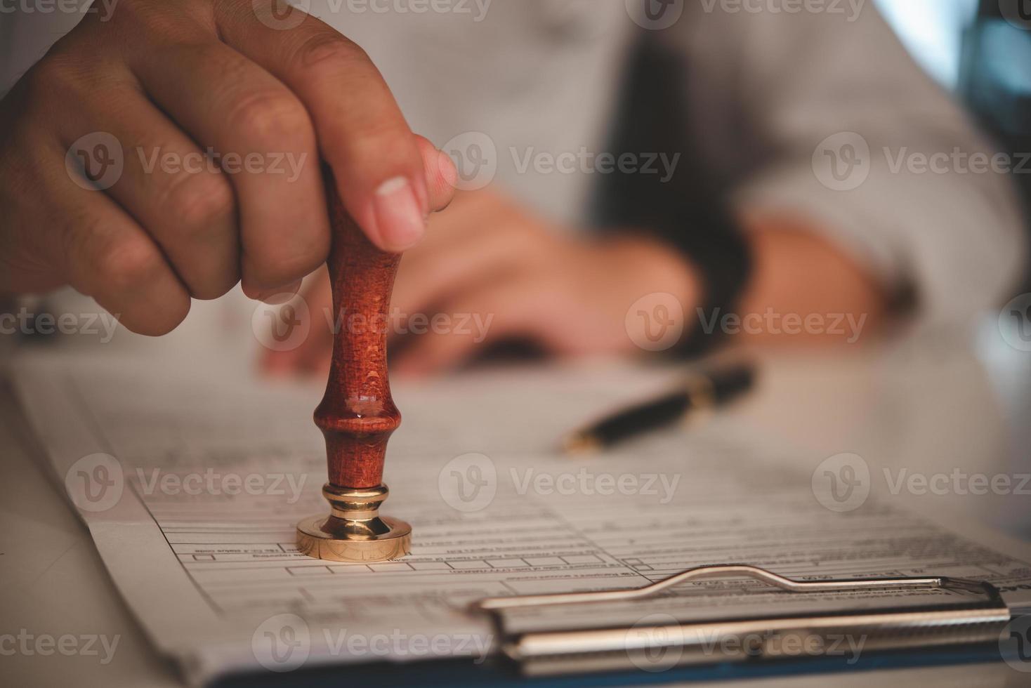 businessman hand stamping approved on certificate document contract in office. Lawyer stamping permit on paperwork at wooden desk. photo