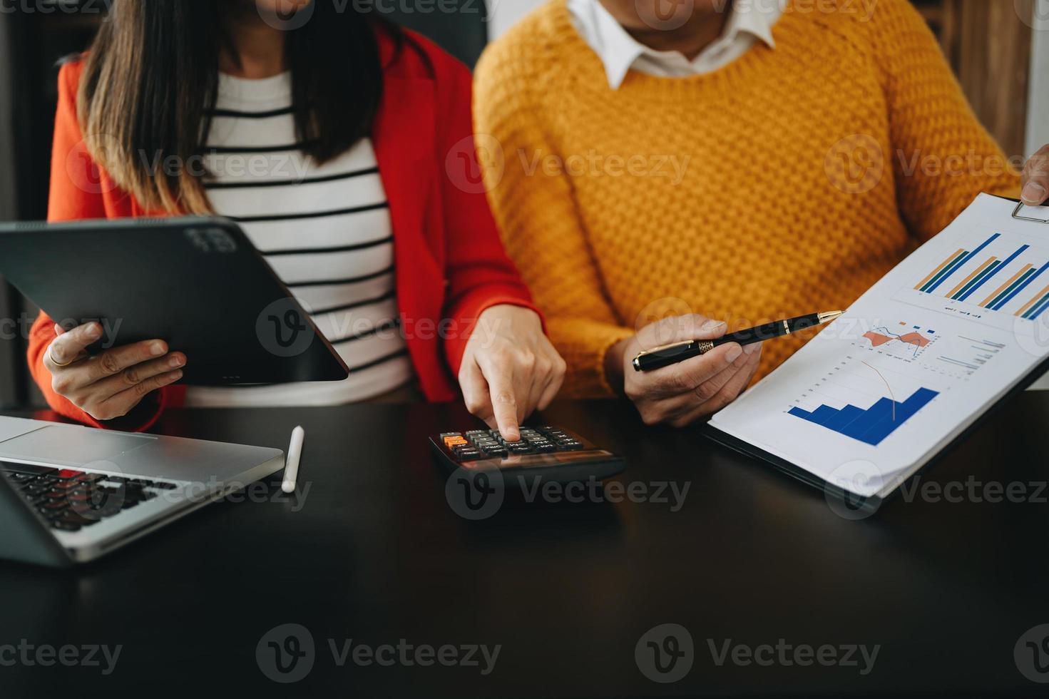 documentos comerciales en la mesa de la oficina con teléfono inteligente y computadora portátil y dos colegas discutiendo datos en segundo plano a la luz de la mañana foto