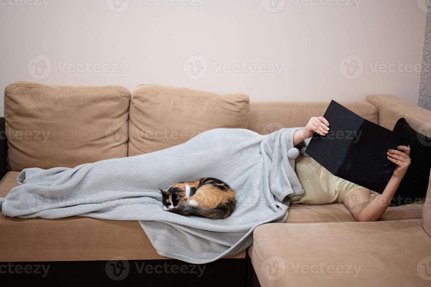 Young woman lying in bed at home and read book with her cat. photo