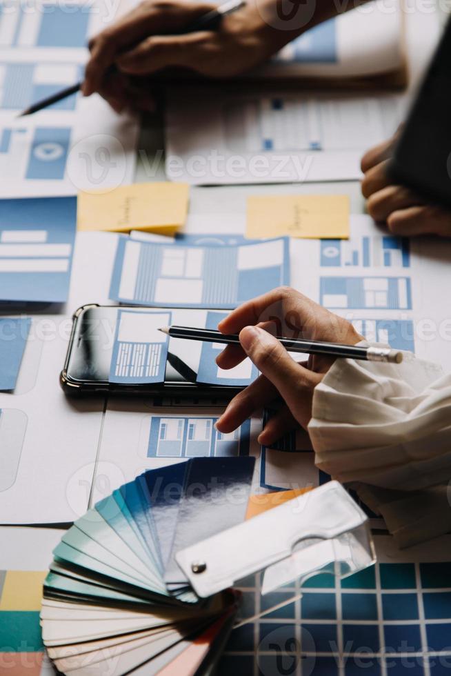 Close up ux developer and ui designer brainstorming about mobile app interface wireframe design on table with customer breif and color code at modern office.Creative digital development agency photo