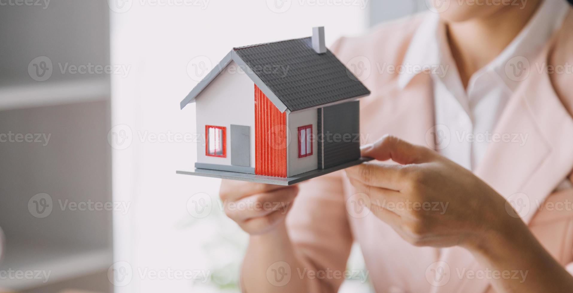 el agente de corretaje de bienes raíces entrega una muestra de una casa modelo al cliente, un contrato de préstamo hipotecario que arrienda y compra una casa y contrata el concepto de seguro de hogar foto
