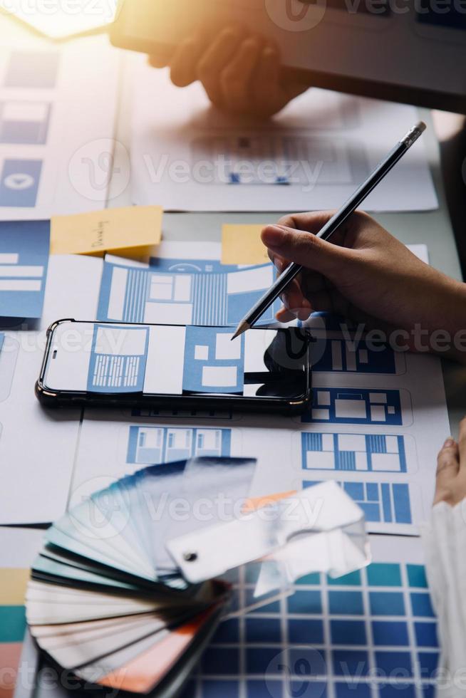Close up ux developer and ui designer brainstorming about mobile app interface wireframe design on table with customer breif and color code at modern office.Creative digital development agency photo