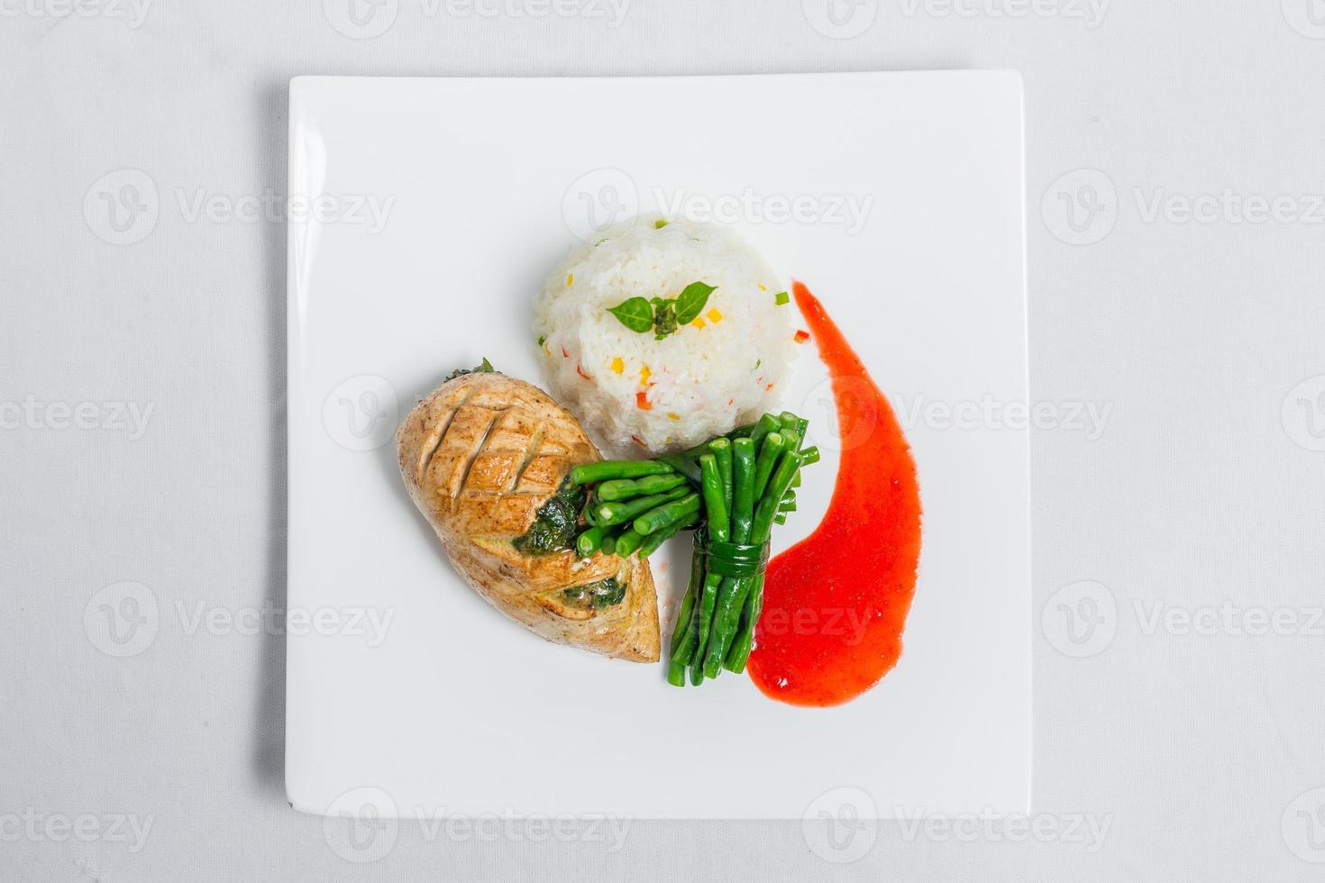 Pan roasted chicken breast with long green beans and light vegetable rice platter. Food decorating with red sauce on a white plate. Isolated white background. photo