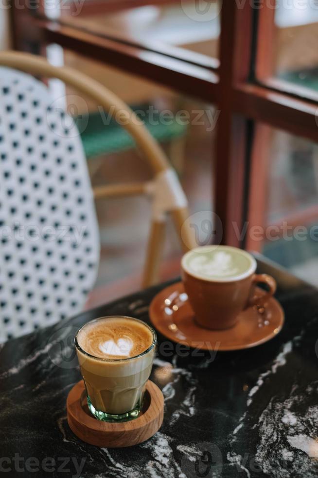 café latté y matcha latté en un negro mármol mesa cerca el ventana foto