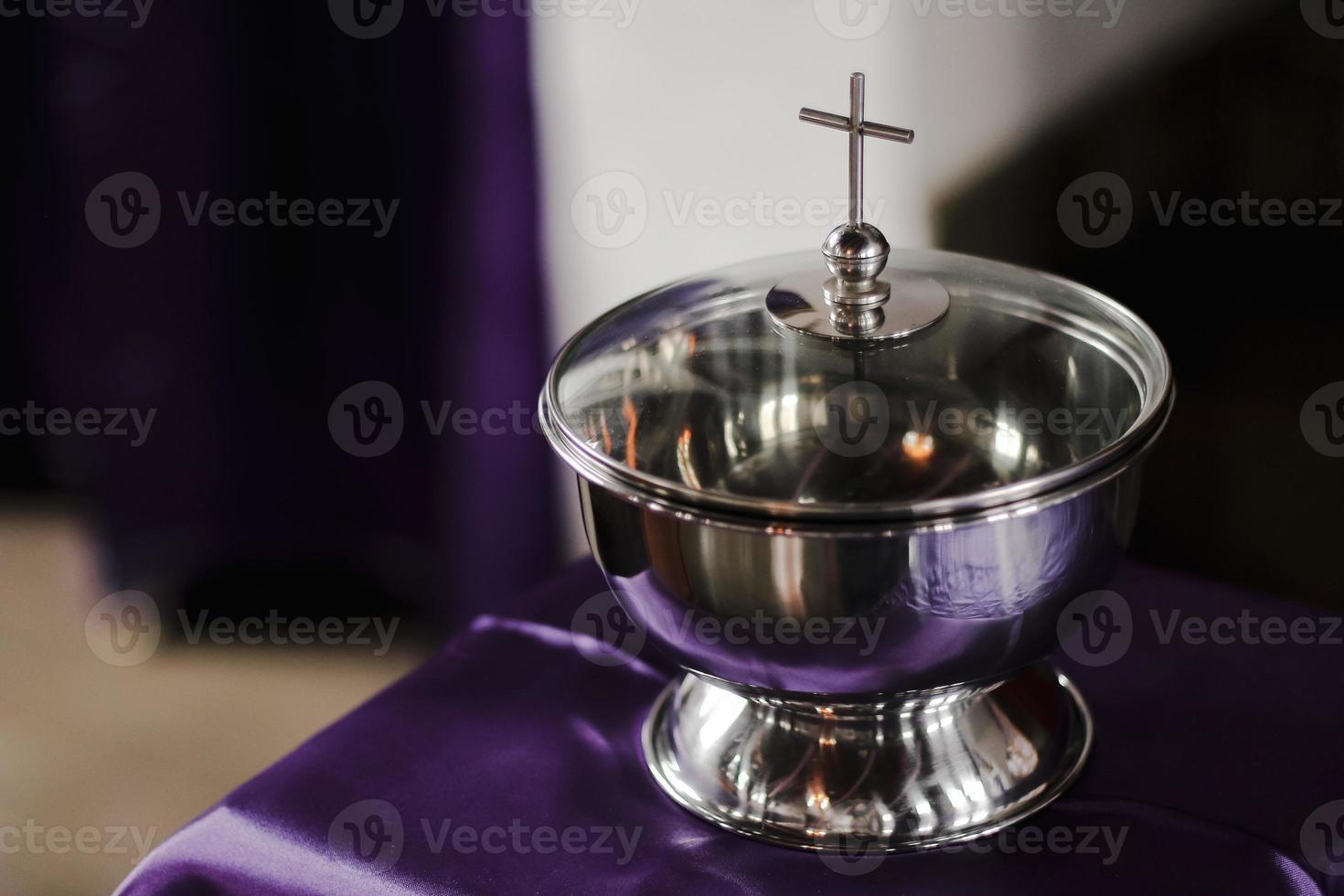 A silver bowl with a cross on it sits on a purple cloth. photo