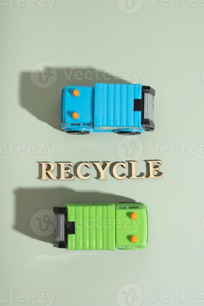 Toy garbage trucks and recycle text on a green background top view, flat lay photo