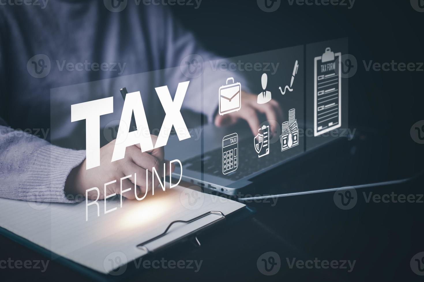 Businessman using a pen to write a notebook with TAX REFUND and refund tax of duty taxation business, graphs and chart being demonstrated on the screen media,  tablet pc and selecting tax refund. photo