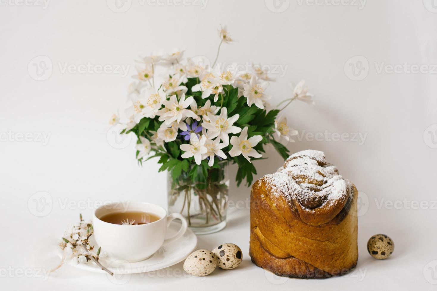 Easter sweet bread, cake and eggs with white apple flowers and primroses, a cup of tea. Festive breakfast concept with copy space. photo
