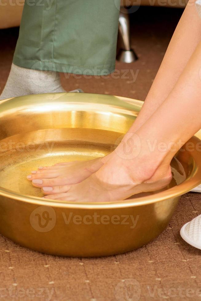 Female feet in a golden bowl with water in spa salon. Spa treatment. photo