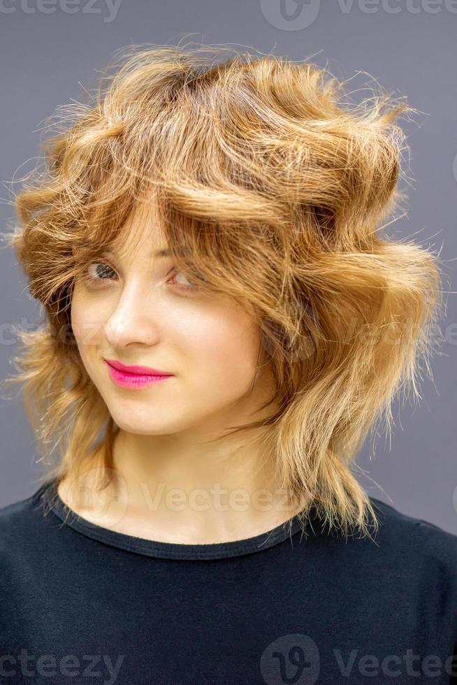 Beautiful young caucasian woman with a red short curly hairstyle on dark background. photo