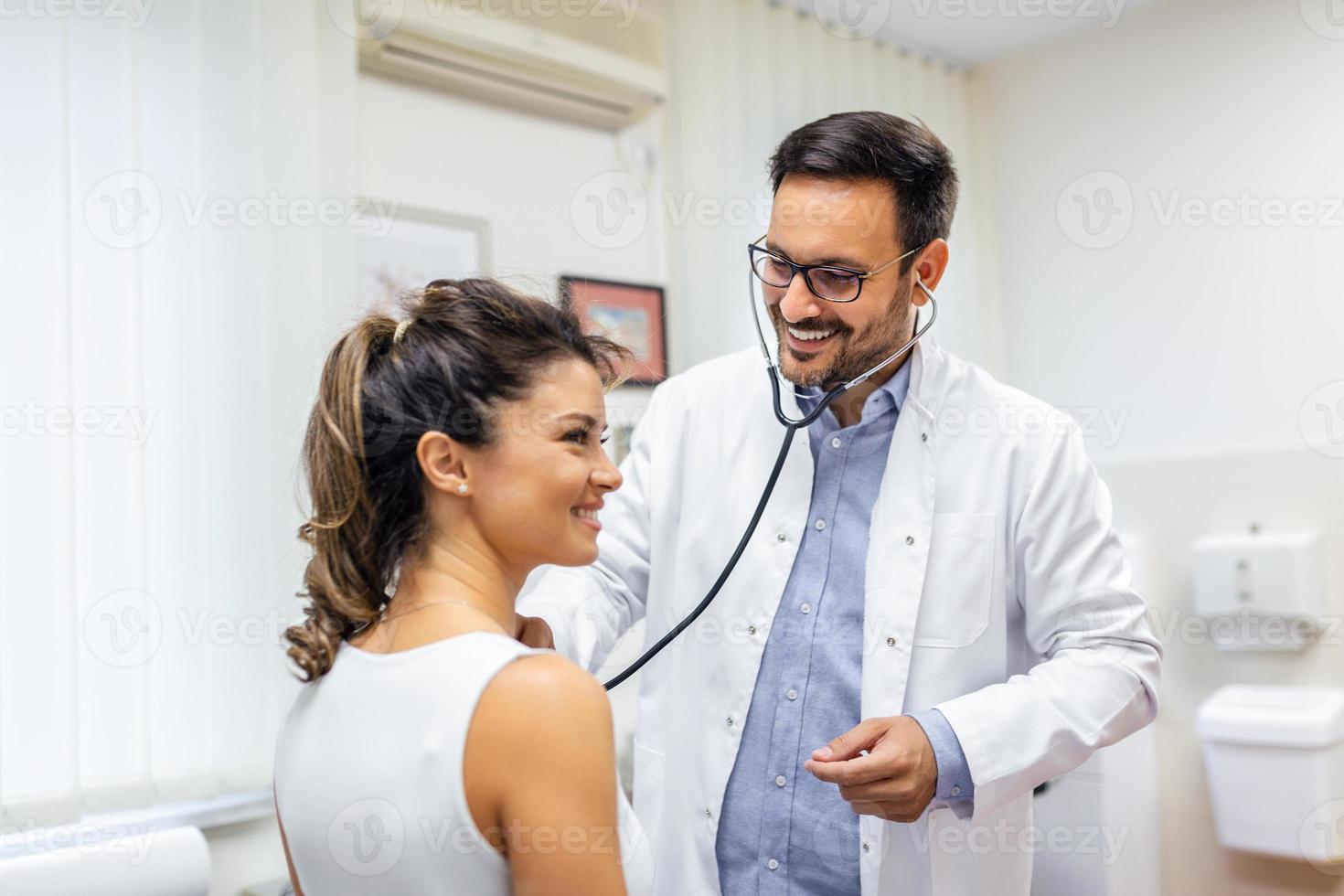 Young doctor listen to female patient heart chest with stethoscope at clinic meeting. Man GP checkup examine woman client with phonendoscope. healthcare concept. photo