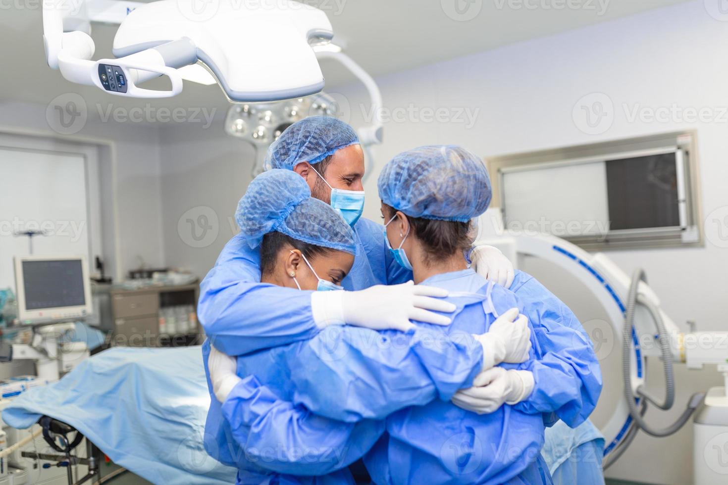 Medical professionals embracing each other in ICU. Doctors and nurses are in protective coveralls after successful treatment. They are at hospital during COVID-19. photo