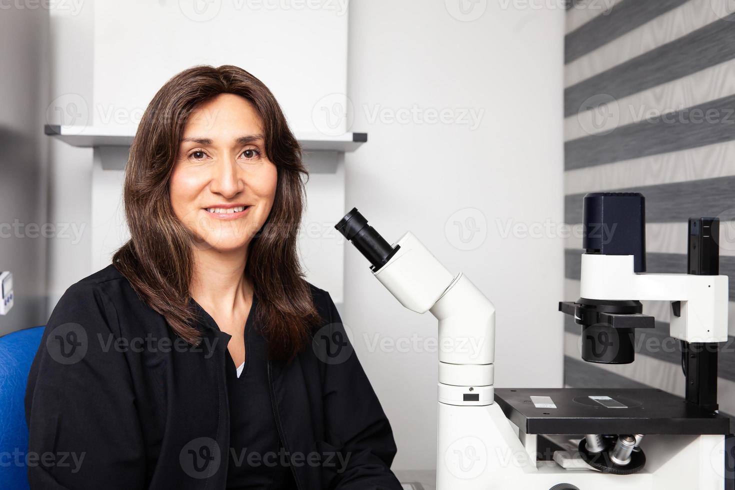 Portrait of a female scientist in the laboratory next to an inverted microscope. photo