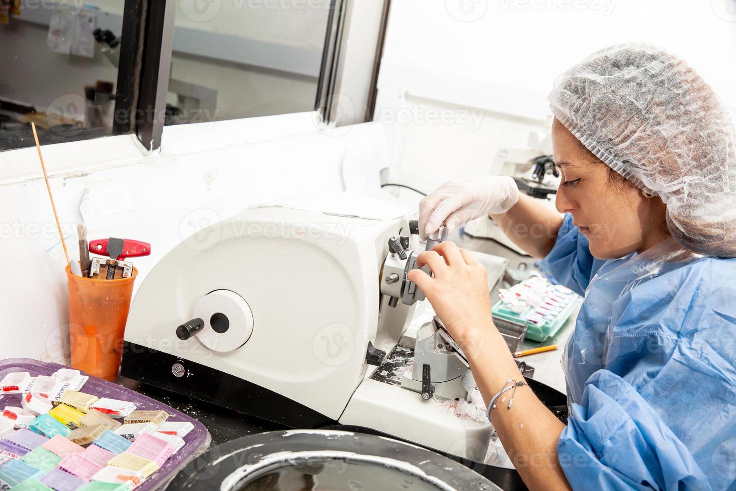 Young female scientist works on a rotary microtome to obtain sections from a paraffin-embedded specimen. photo
