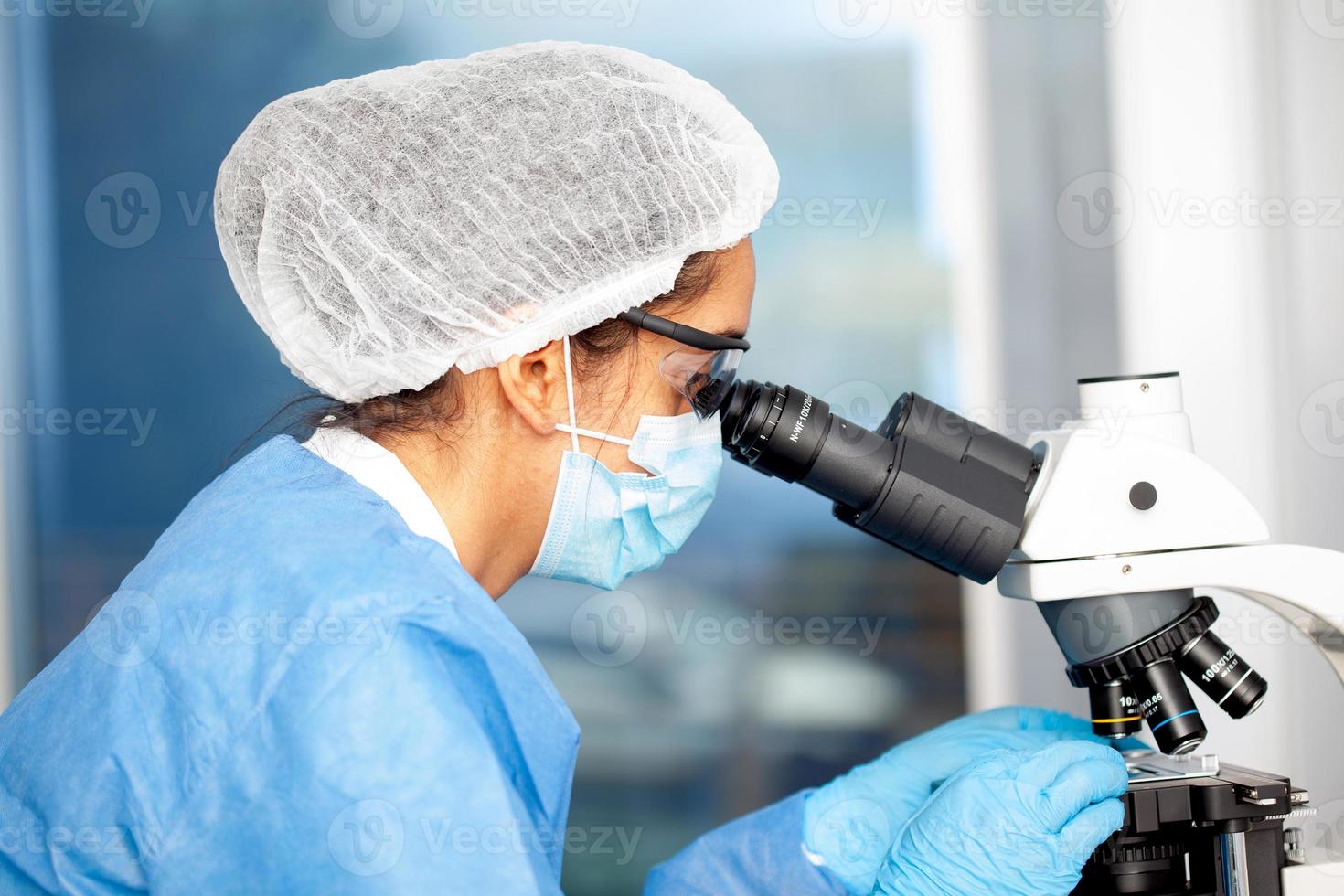joven hembra científico mirando a muestras debajo el microscopio foto