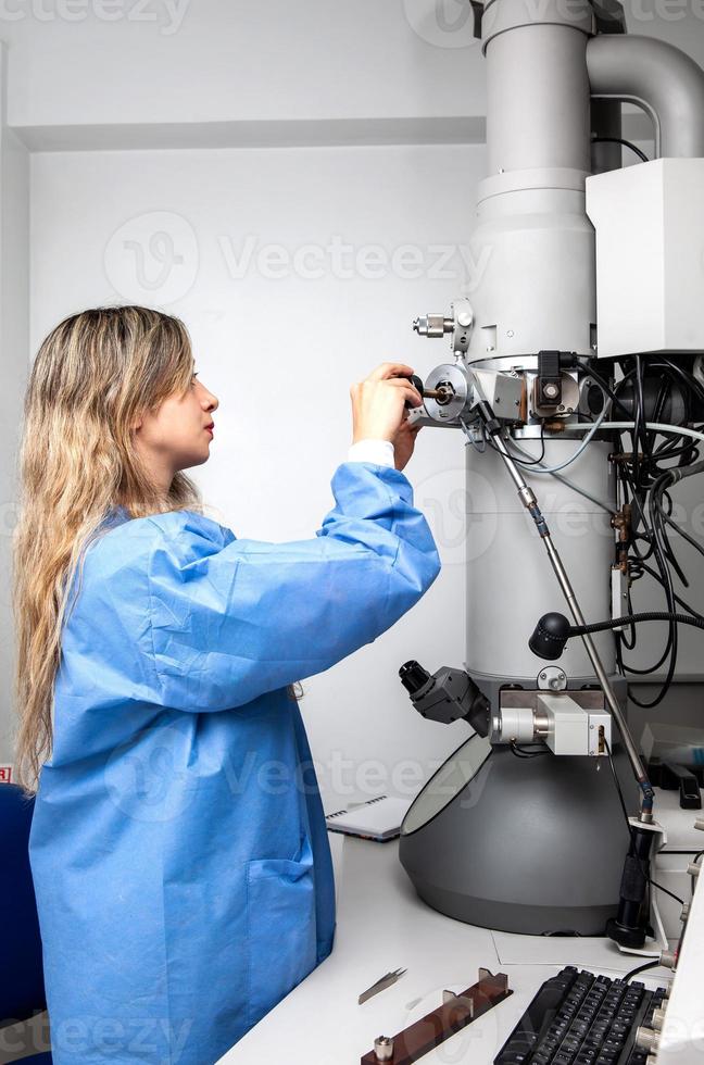 Young female scientist loading a specimen using a sample holder into a transmission electron microscope photo