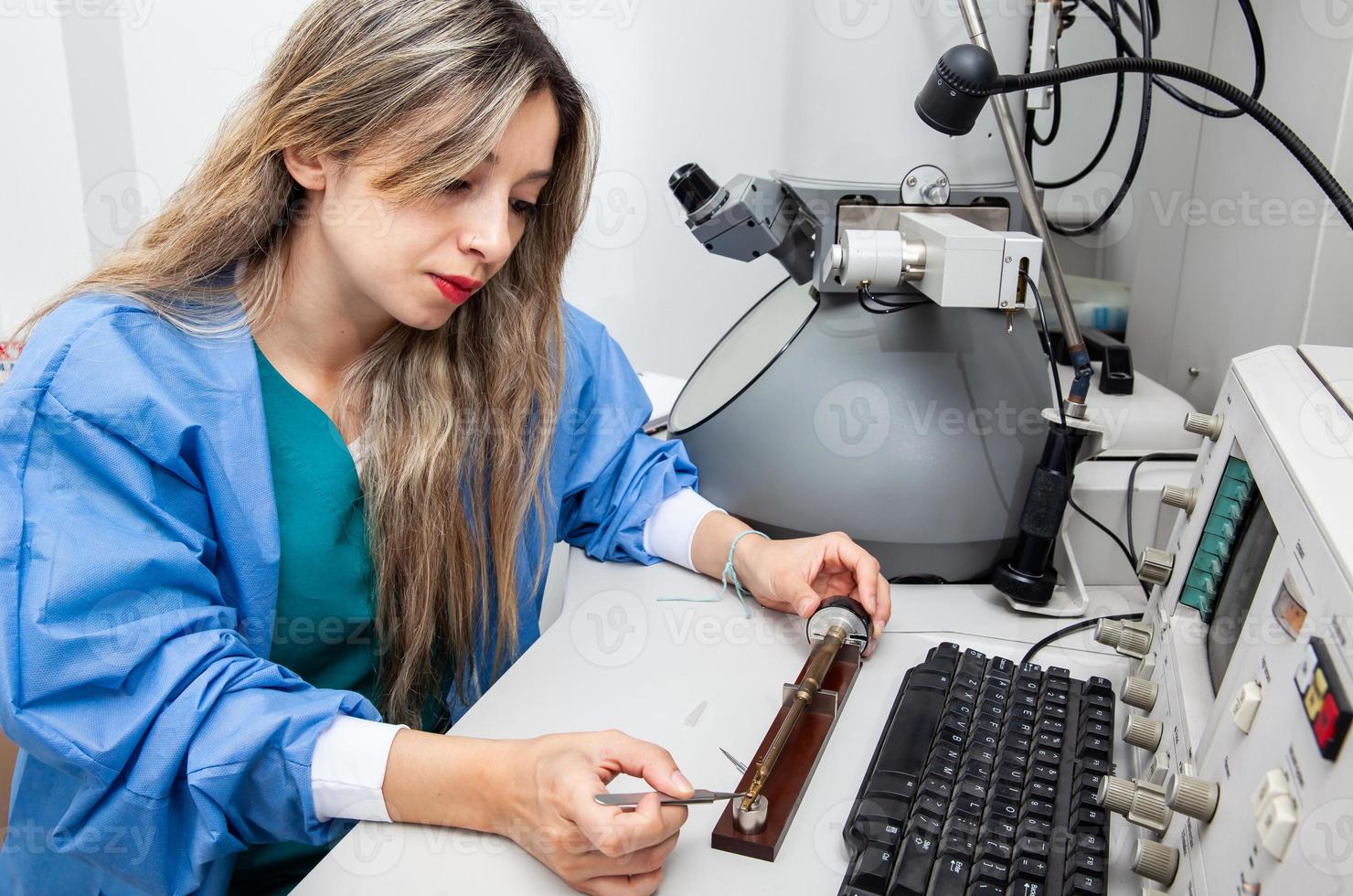 Young female scientist loading a grid with an specimen on the sample holder of a transmission electron microscope photo