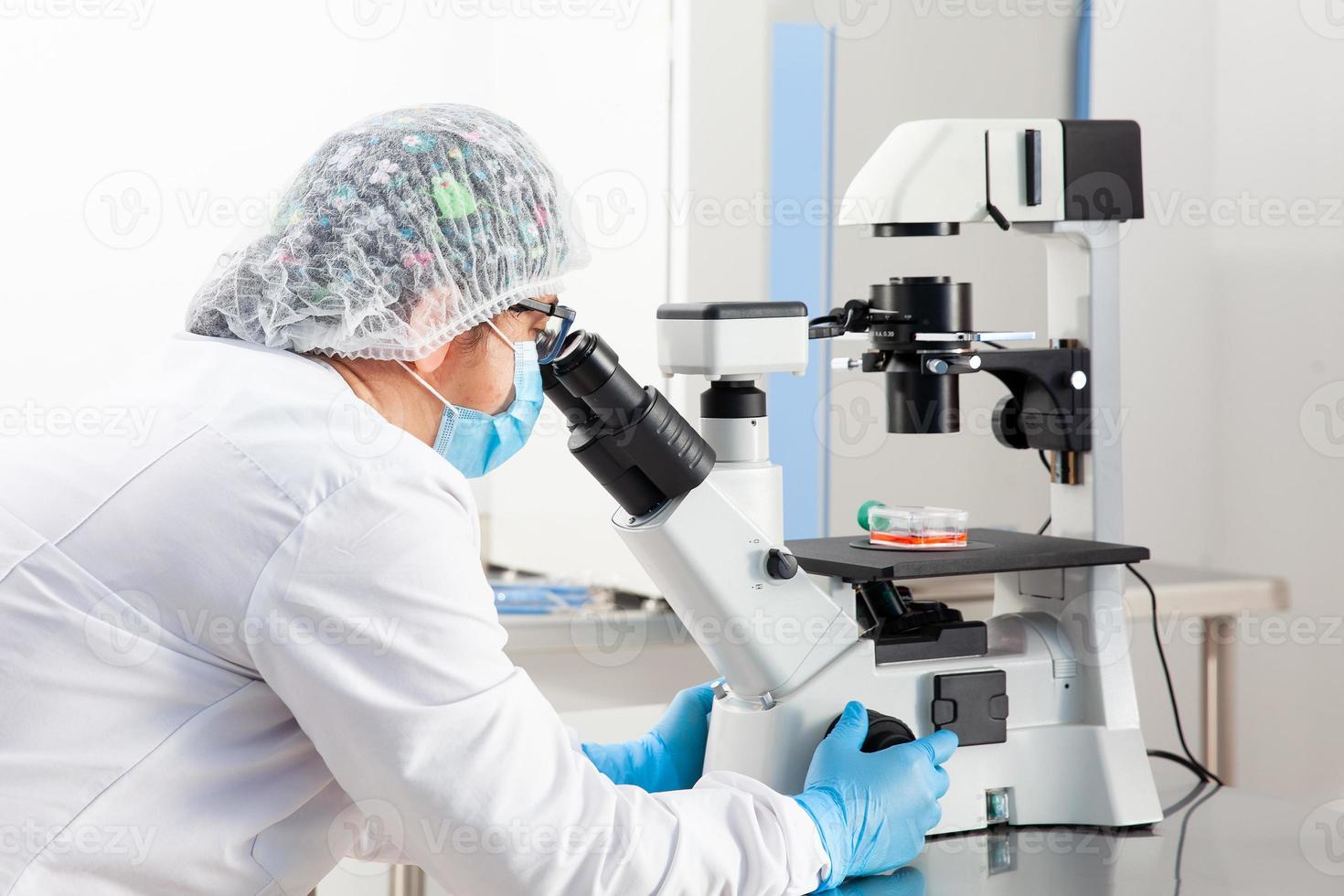 Young female scientist looking at samples under the microscope photo