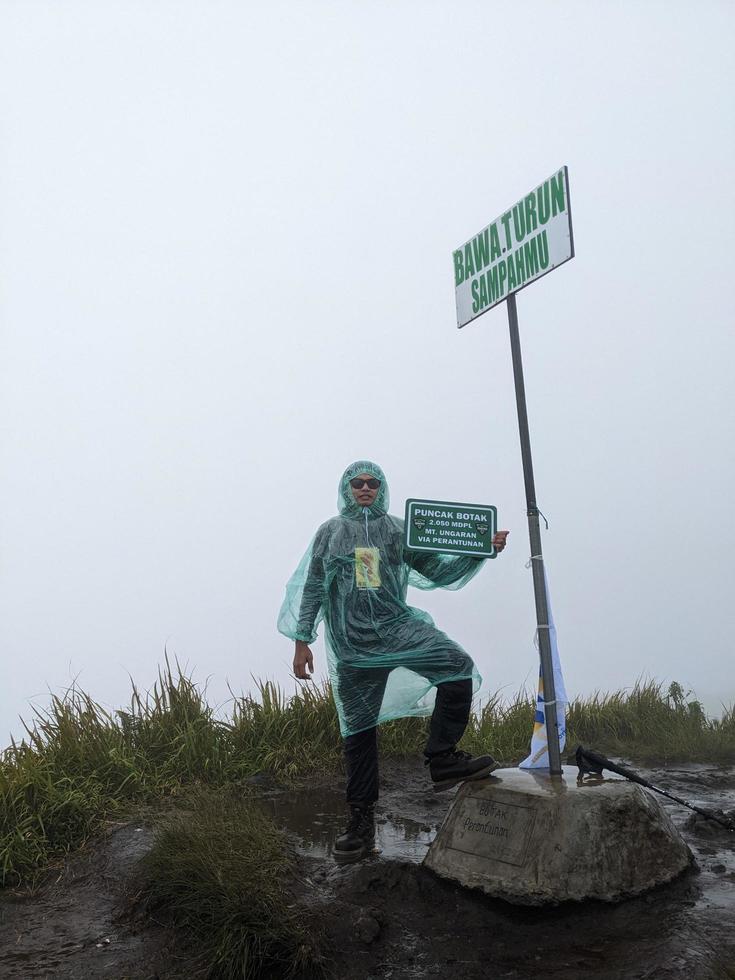 Man reach peak of mountain when rainy day with foggy vibes. The photo is suitable to use for adventure content media, nature poster and forest background.