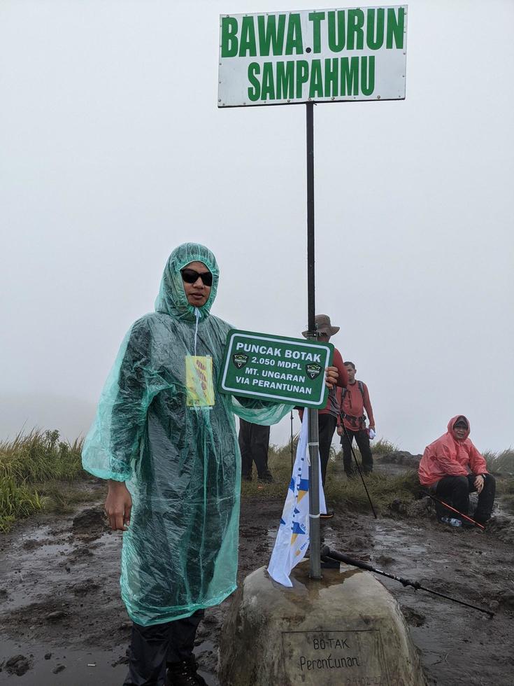 Man reach peak of mountain when rainy day with foggy vibes. The photo is suitable to use for adventure content media, nature poster and forest background.