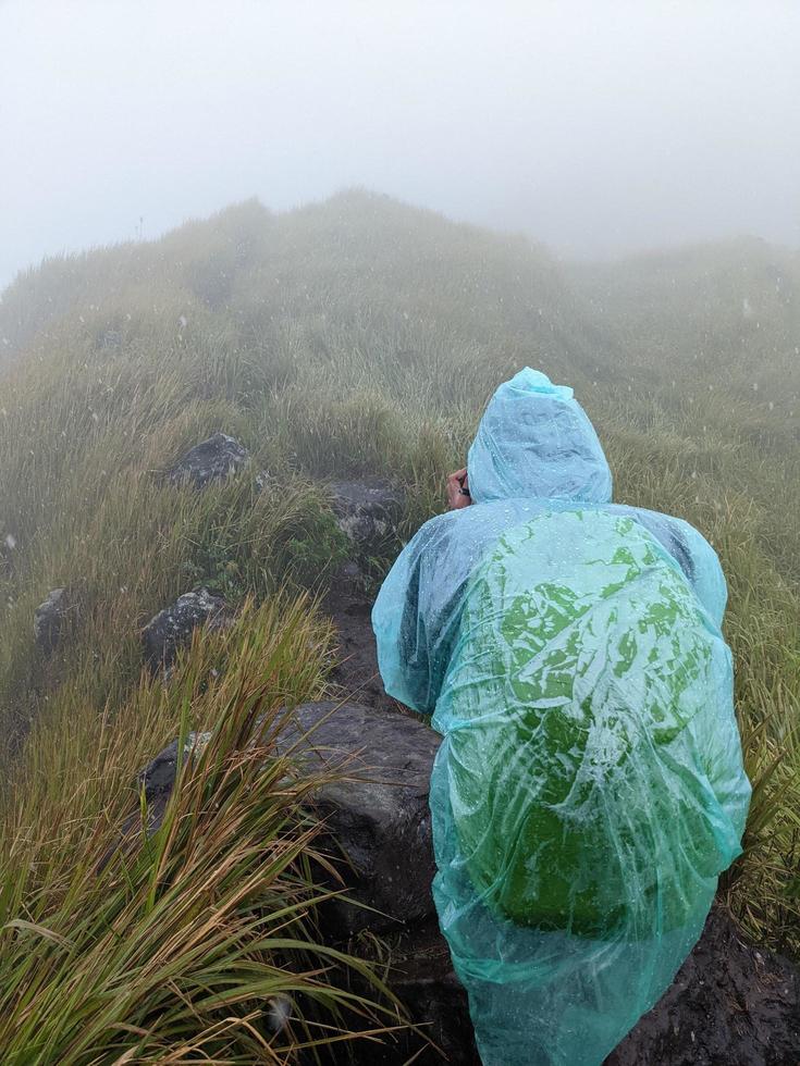 Man reach peak of mountain when rainy day with foggy vibes. The photo is suitable to use for adventure content media, nature poster and forest background.