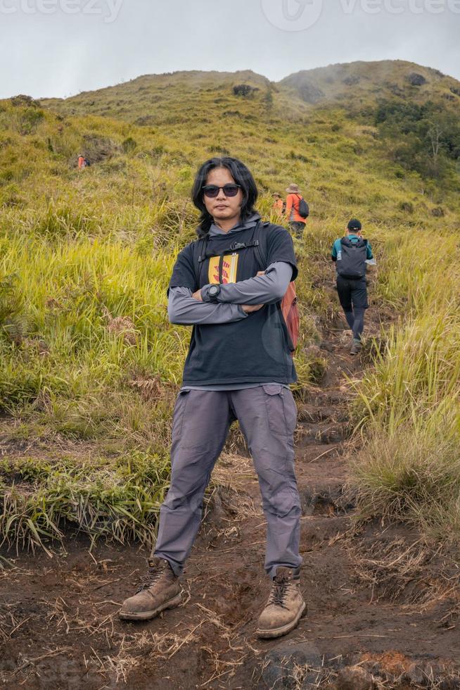 Man hiking to the top mountain, with Savana track and cloudy vibes. The photo is suitable to use for adventure content media, nature poster and forest background.