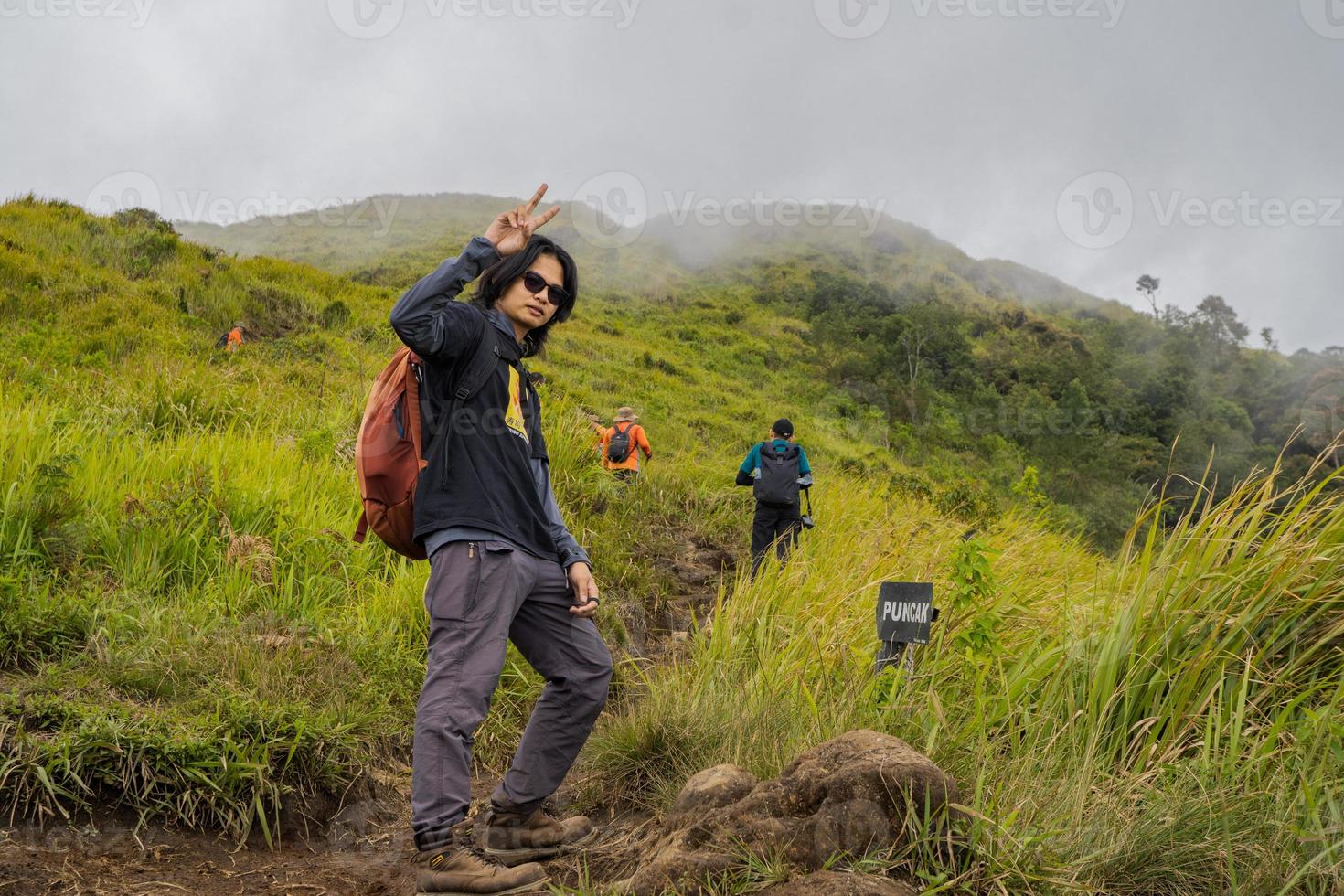 Man hiking to the top mountain, with Savana track and cloudy vibes. The photo is suitable to use for adventure content media, nature poster and forest background.