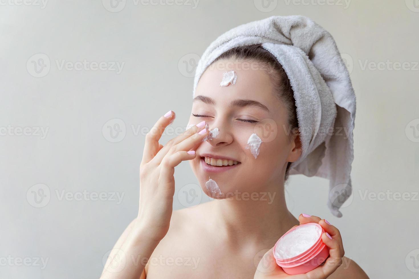 Beauty portrait of woman in towel on head with white nourishing mask or creme on face, white background isolated photo