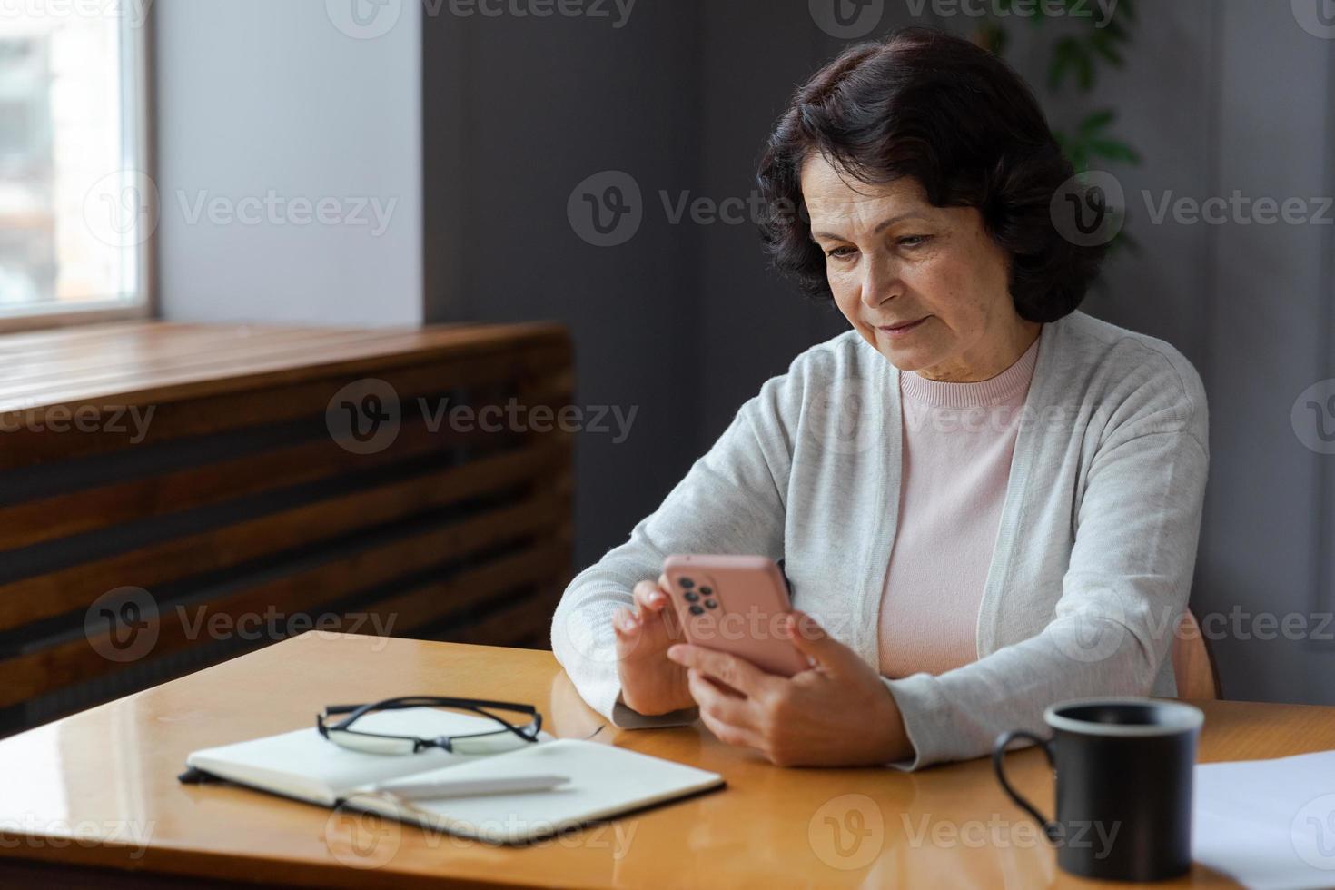 European middle aged senior woman holding using smartphone touch screen typing scroll page. Stylish older mature 60s lady with cell phone using internet social media apps at home. Shopping online. photo
