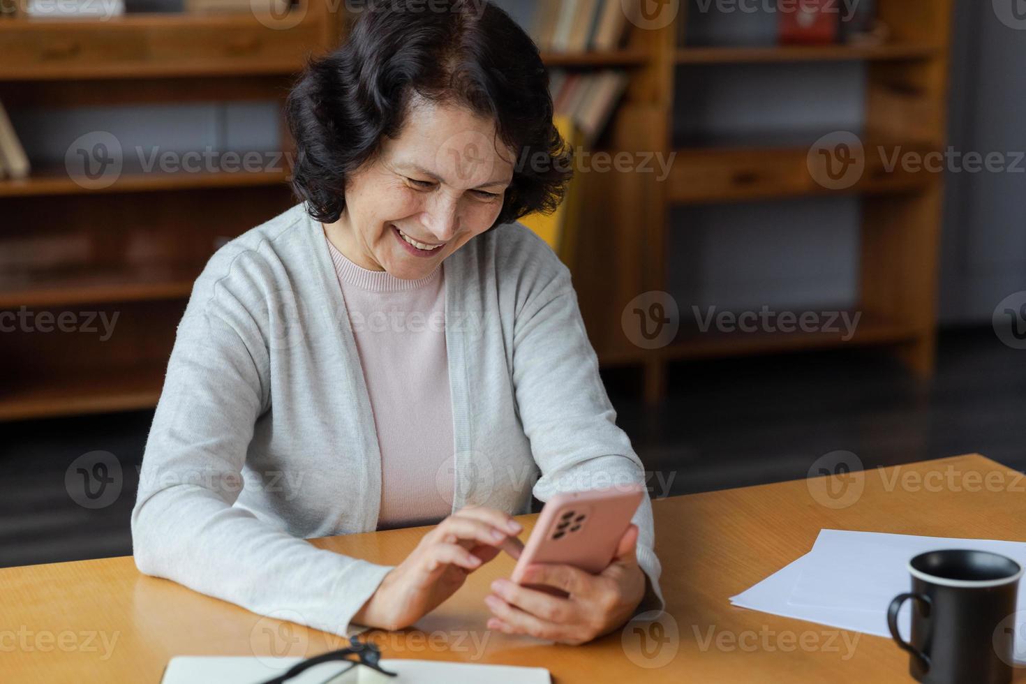 European middle aged senior woman holding using smartphone touch screen typing scroll page. Stylish older mature 60s lady with cell phone using internet social media apps at home. Shopping online. photo