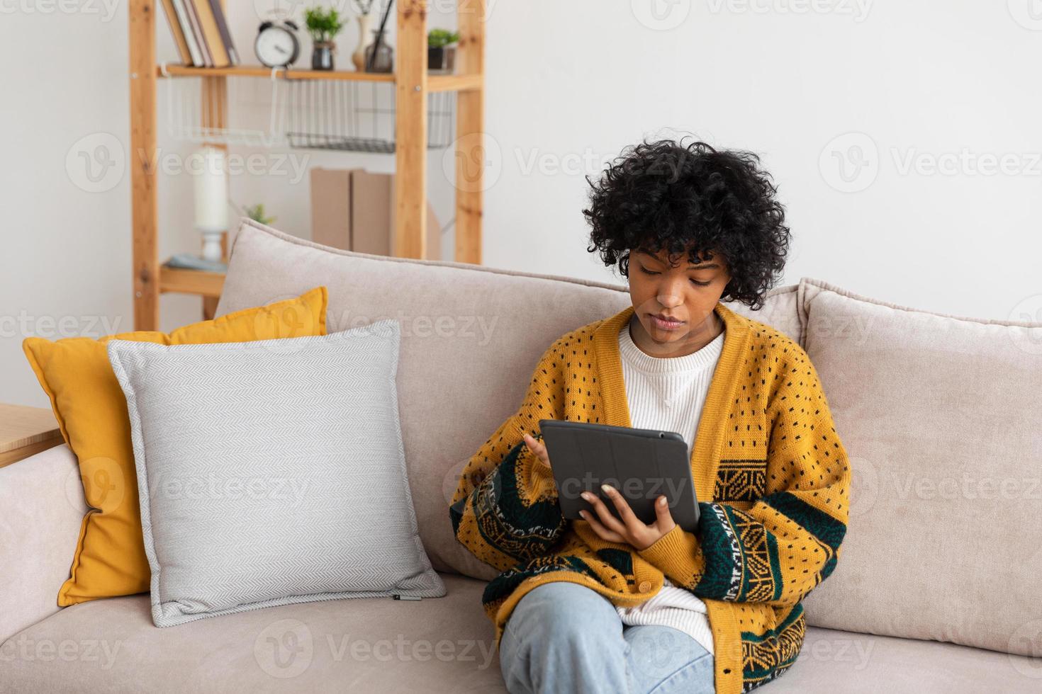 African american girl holding digital tablet touch screen typing scroll page at home. Woman with mobile tech device surfing internet using social media apps playing game. Study work shopping online. photo