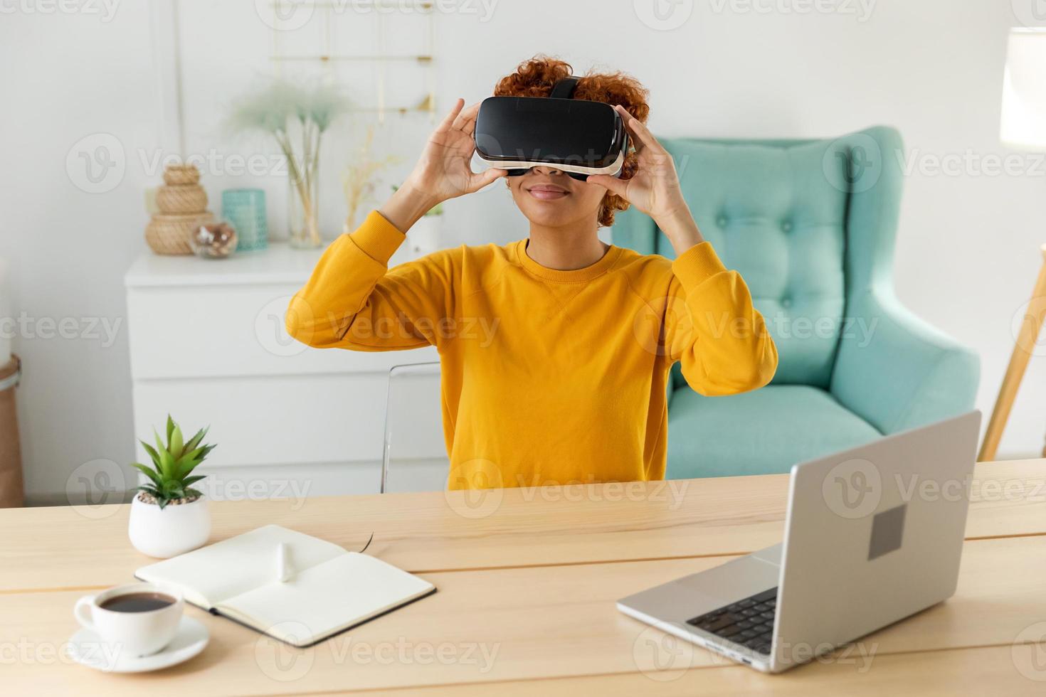 African american young woman wearing using virtual reality metaverse VR glasses headset at home. Girl puts on virtual reality helmet. Technology simulation hi-tech videogame concept. photo