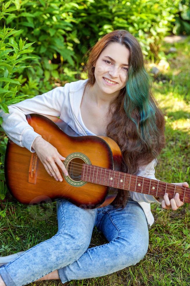 Young woman sitting in grass and playing guitar photo