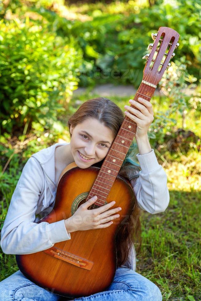 Young woman sitting in grass and playing guitar photo